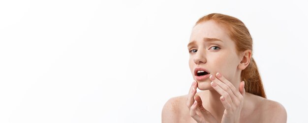 Mujer pelirroja muestra los dedos sobre el acné en la cara