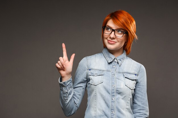 Mujer pelirroja pensativa apuntando hacia arriba