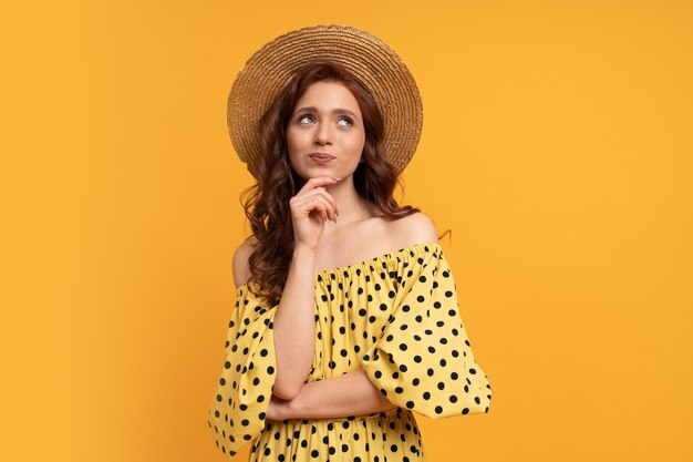 Mujer pelirroja pensativa posando en vestido amarillo con mangas en amarillo. Estado de ánimo de verano.