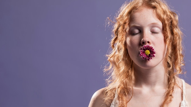 Mujer pelirroja posando con una flor sobre su boca y copia espacio