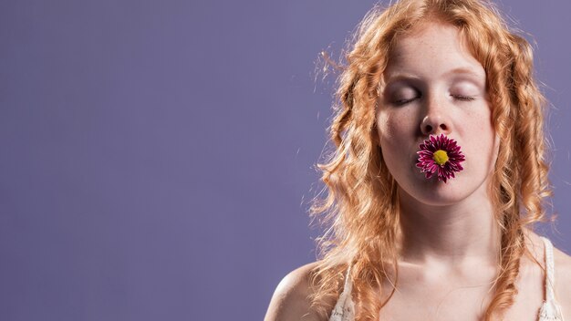 Mujer pelirroja posando con una flor sobre su boca y copia espacio