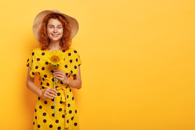 Mujer pelirroja posando en vestido de lunares amarillo y sombrero de paja