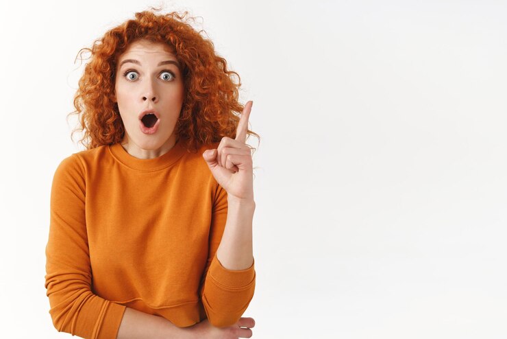 Foto gratuito mujer pelirroja y preciosa, sorprendida y emocionada, tiene una idea excelente. una compañera de trabajo comparte sus ideas con el equipo, jadea con la boca abierta porque ha tenido un plan impresionante y levanta el dedo con un gesto de ¡eureka!