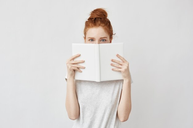 Mujer pelirroja que oculta la cara detrás del cuaderno asustada.