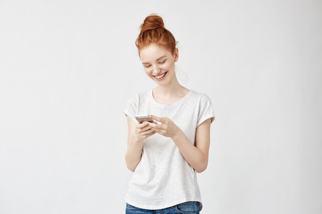 Mujer pelirroja sincera sonriendo mirando el teléfono.