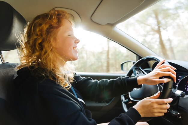 Mujer pelirroja sonriente que conduce el coche