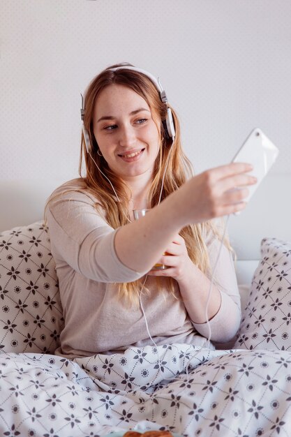 Mujer pelirroja tomando selfie en la cama