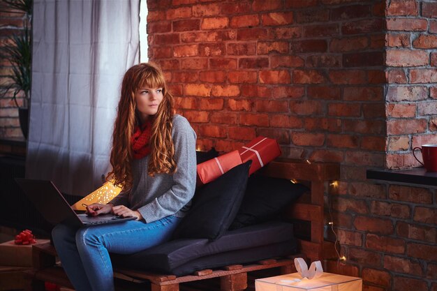 Mujer pelirroja usando una computadora portátil en una habitación con interior tipo loft.