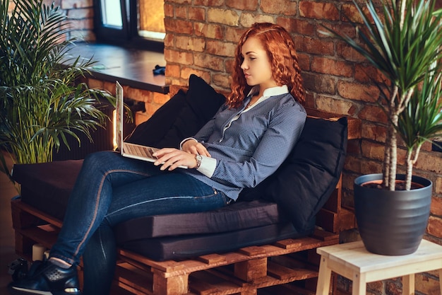 Mujer pelirroja usando una computadora portátil en una sala de estar con interior de loft.