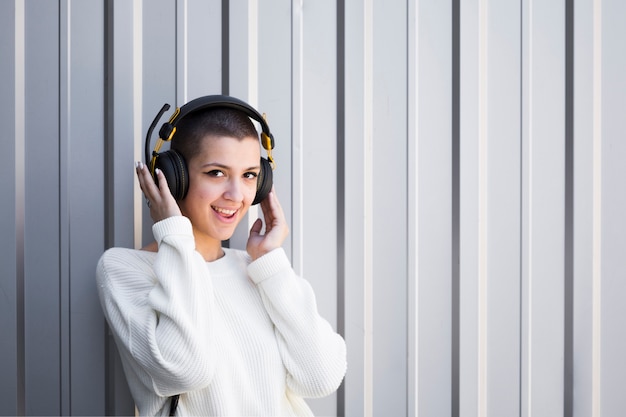 Mujer con pelo corto escuchando música en auriculares y mirando a cámara