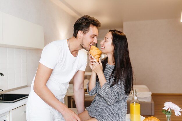 Mujer de pelo largo alimentando novio con croissant y sonriendo