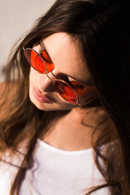 Mujer con el pelo largo en gafas de sol rojas se sienta en la arena blanca