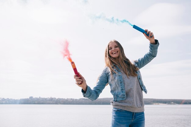 Mujer de pelo largo sonriente sosteniendo bombas de humo de colores