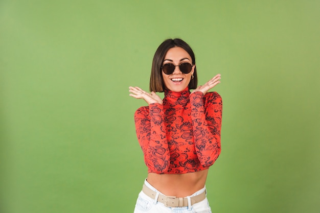 Mujer de pelo muy corto con aretes dorados, gafas de sol, blusa estampada de dragón de china roja sobre verde