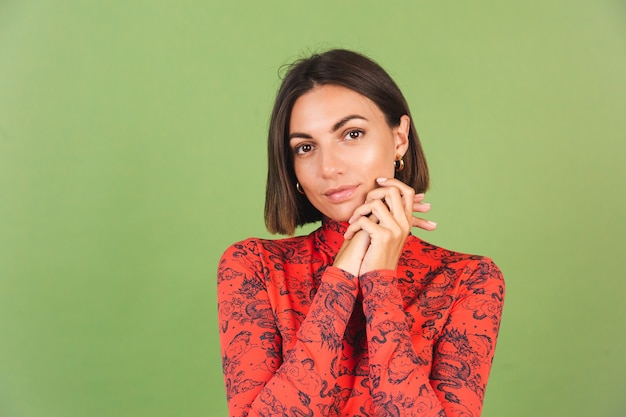 Mujer de pelo muy corto con maquillaje ligero aretes dorados blusa estampada de dragón chino rojo en verde, emociones positivas, sonrisa segura