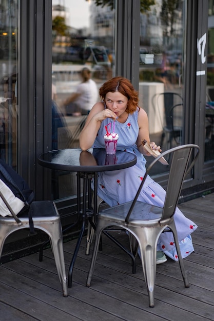 mujer con pelo rojo en un café bebe un cóctel de verano, feliz, ríe, sonríe.