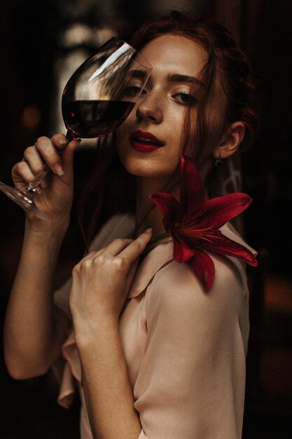 Mujer de pelo rojo posando con flor y copa de vino