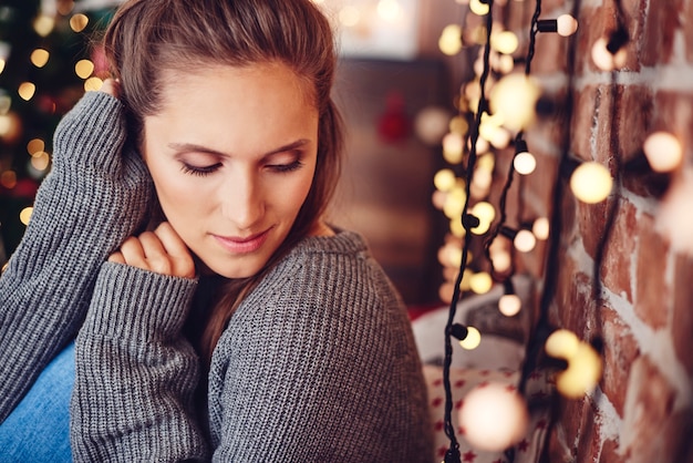 Mujer pensando en casa con luces de Navidad en la pared