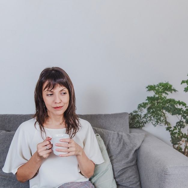 Mujer pensativa con café en el sofá