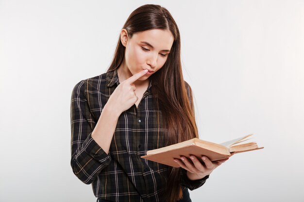 Mujer pensativa en camisa leyendo libro