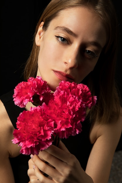 Mujer pensativa con claveles rosados.