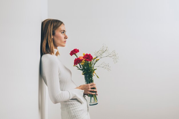 Mujer pensativa con flores en florero en pared