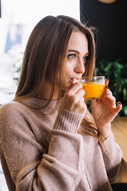 Mujer pensativa joven elegante que bebe de la taza en café