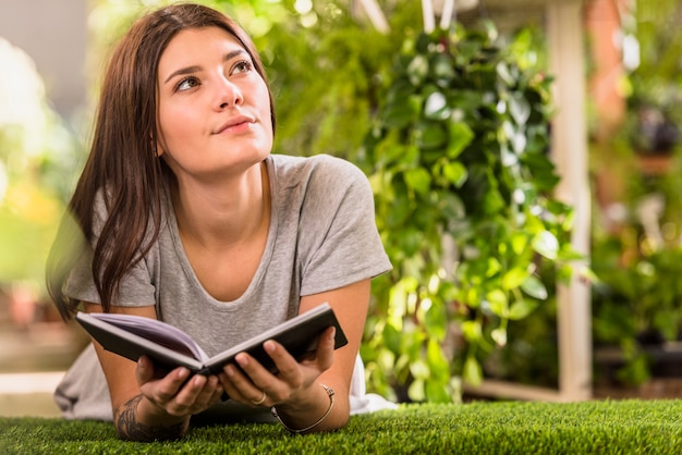 Mujer pensativa joven con el libro que miente en césped