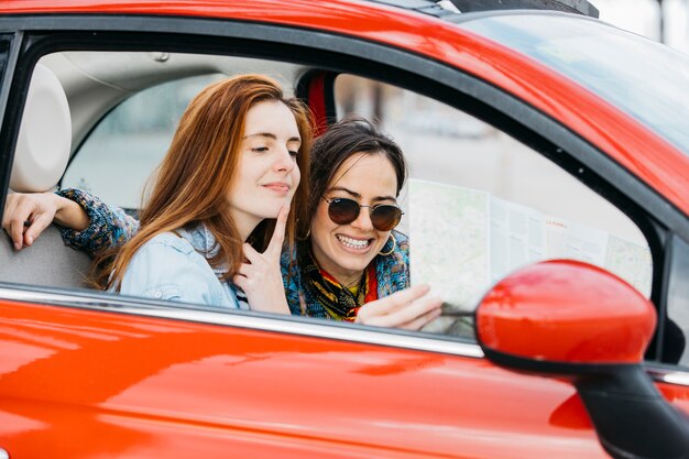 Mujer pensativa joven y señora sonriente que se sienta en coche y que mira el mapa