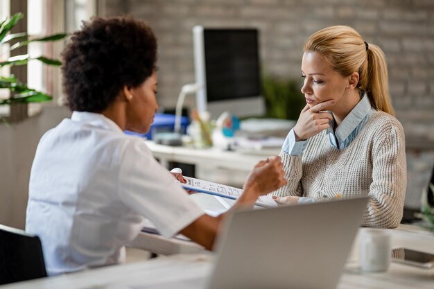 Mujer pensativa pasando por los resultados de las pruebas médicas con su médico en la clínica