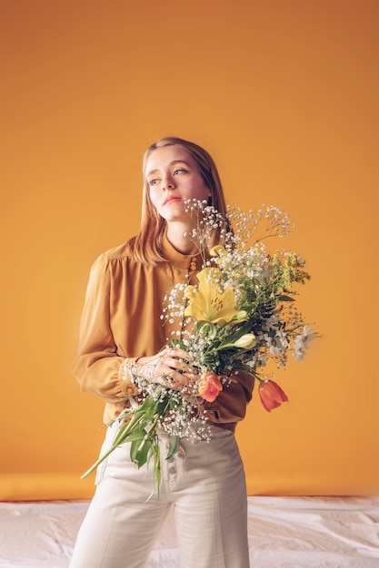 Mujer pensativa de pie con ramo de flores