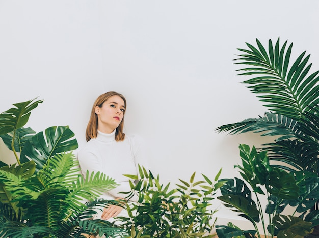 Mujer pensativa que se coloca cerca de las plantas verdes