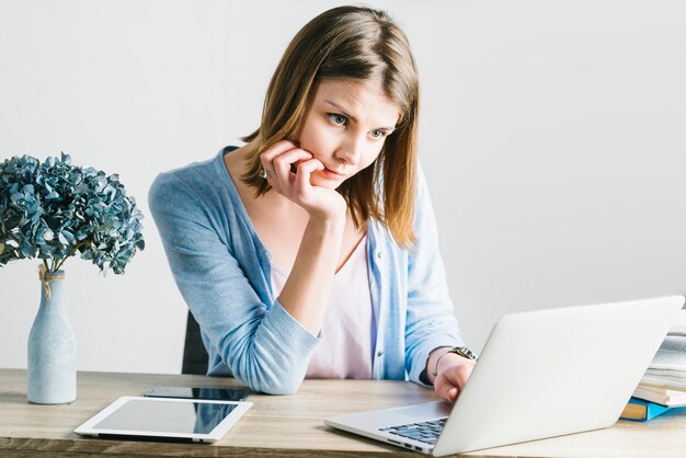 Mujer pensativa que hojea la computadora portátil en oficina