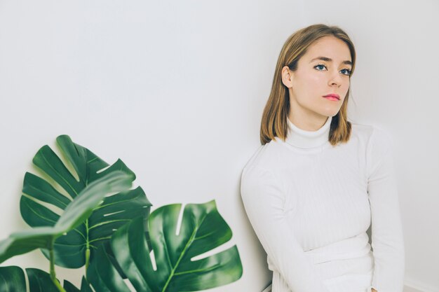 Mujer pensativa que se sienta cerca de la planta verde