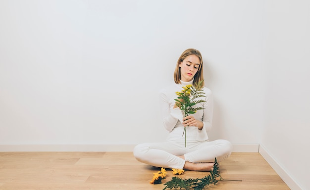 Foto gratuita mujer pensativa que se sienta con las ramas de la planta en piso