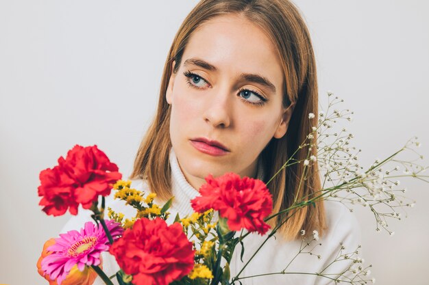 Mujer pensativa que sostiene las flores coloridas