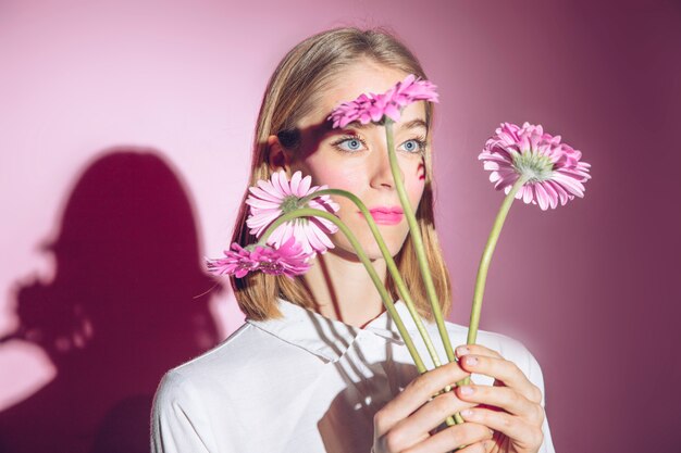 Mujer pensativa que sostiene las flores rosadas del gerbera