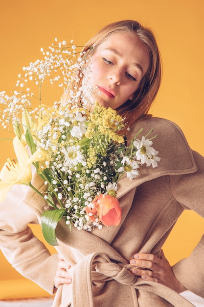 Mujer pensativa con ramo de flores grandes en abrigo