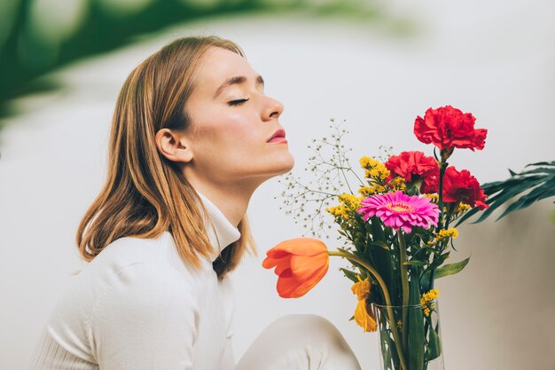 Mujer pensativa sentada con flores brillantes en florero