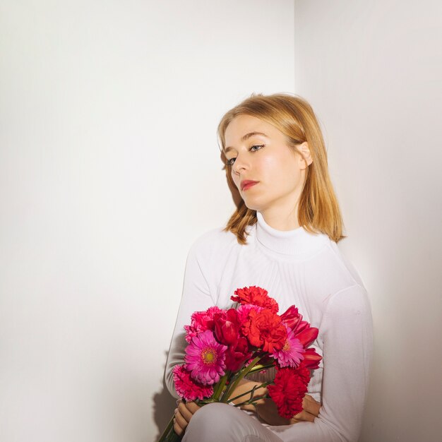 Mujer pensativa sentada con flores brillantes