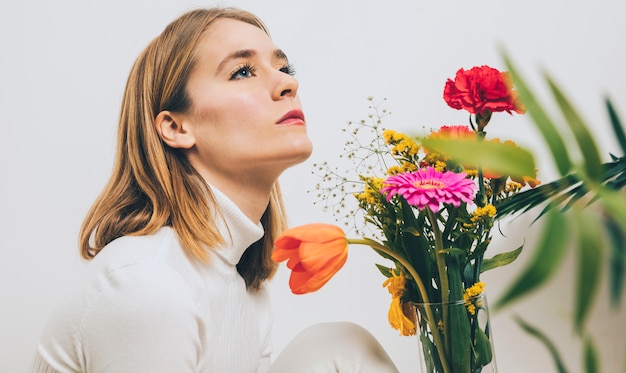 Mujer pensativa sentada con flores en florero