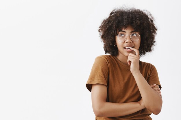 Mujer pensativa y soñadora pensando en lo que desea y quiere morderse la uña con expresión intrigada e interesada mirando la esquina superior izquierda