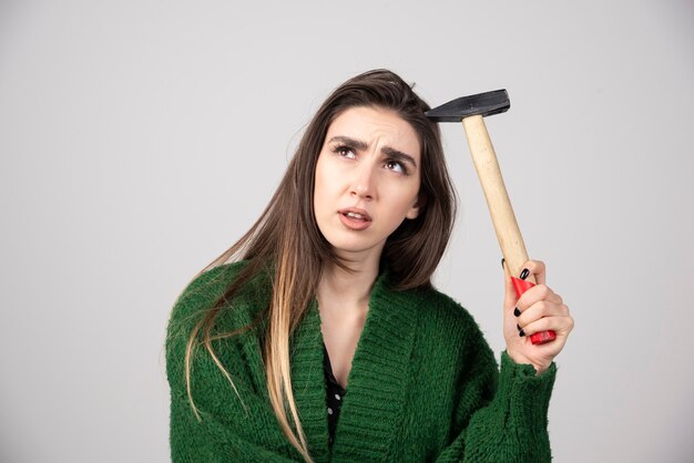 Mujer pensativa sosteniendo un martillo en las manos sobre un fondo gris.