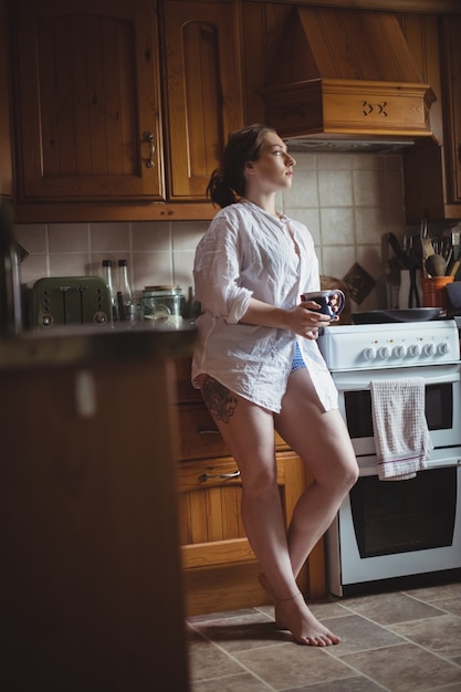 Foto gratuita mujer pensativa sosteniendo la taza de café en la cocina