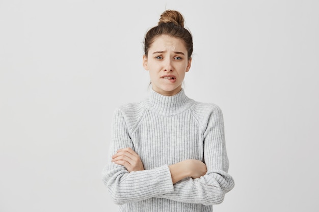 Mujer perpleja con ropa casual de pie con los brazos cruzados. Mujer mujer mordiendo los labios con sentimientos de arrepentimiento sobre el trabajo. Concepto de emociones