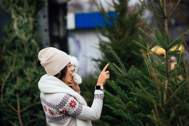 Mujer con un perro blanco en sus brazos cerca de un verde árboles de Navidad en el mercado