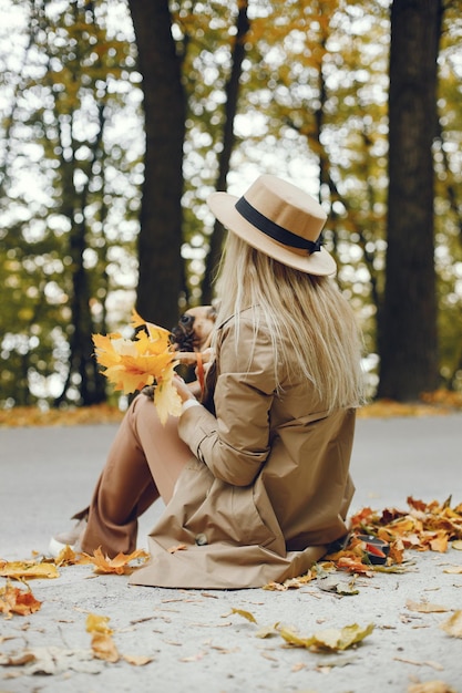 Mujer y perro recogiendo hojas en el parque de otoño