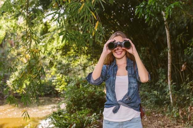 Mujer de pie en el bosque mirando a través de binoculares