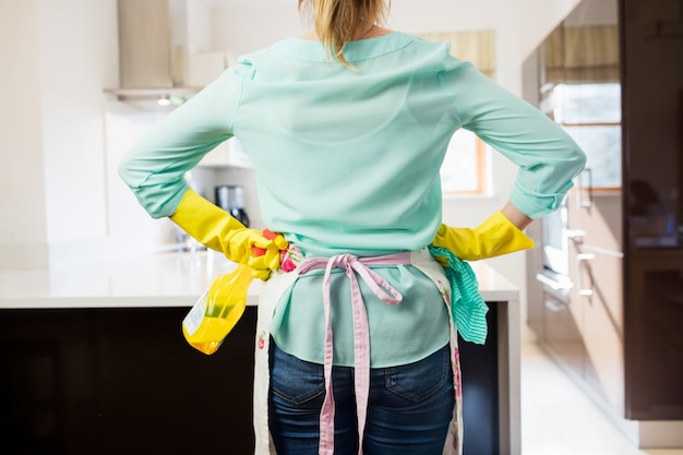 Mujer de pie con la botella del aerosol y servilleta en la cocina