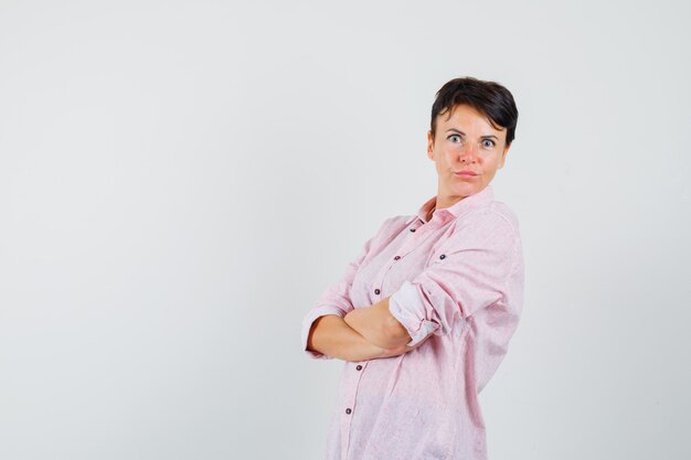 Mujer de pie con los brazos cruzados en camisa rosa y mirando enfocado. vista frontal.